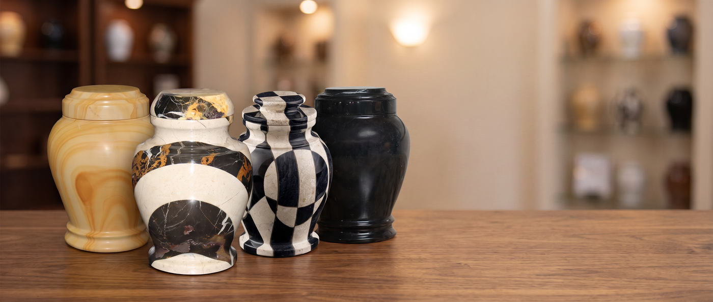 Four decorative ceramic urns in various patterns and colors, including black and white checkered, black and white marble, and solid black, arranged on a wooden table with a blurred indoor background.